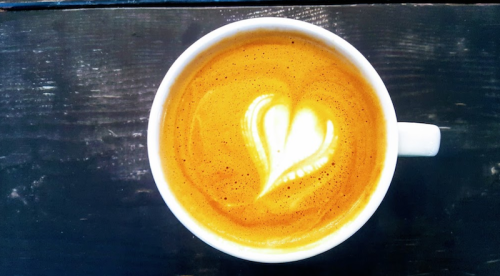 A close-up of a cup of coffee with a heart-shaped latte art design on top, set against a dark wooden surface.