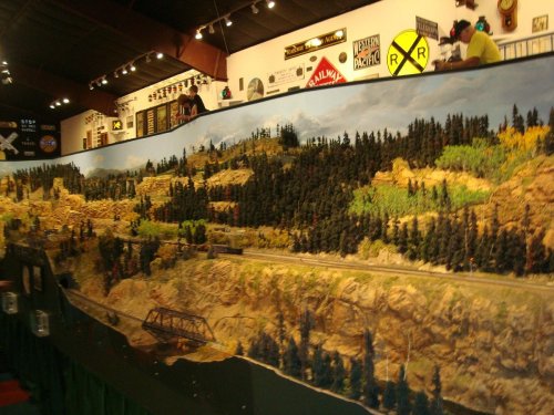 A detailed model train layout featuring mountains, forests, and a railway track in a display room.