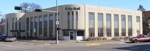 City Hall building with a modern design, featuring large windows and a public power sign, located at a street intersection.