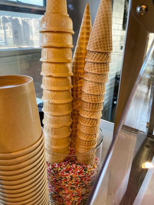 A glass filled with colorful sprinkles and stacked ice cream cones on display.
