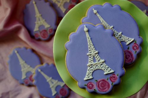 Decorative cookies with purple icing, featuring Eiffel Tower designs and rose accents on a green plate.
