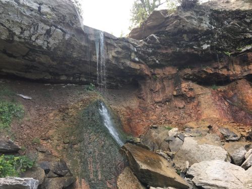 A waterfall cascading down a rocky cliff, surrounded by earthy tones and scattered boulders.