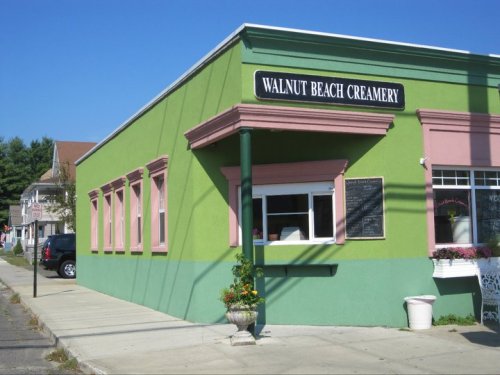 Colorful exterior of Walnut Beach Creamery, featuring green walls and pink trim, with a sidewalk and street view.