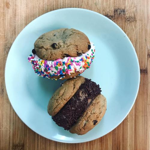 Two cookie sandwiches on a light blue plate: one with sprinkles and frosting, the other with chocolate sprinkles.