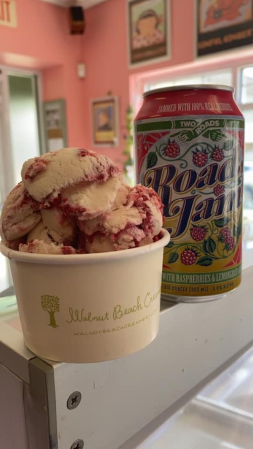 A cup of raspberry swirl ice cream next to a can of Two Roads Road Jam beer on a counter.
