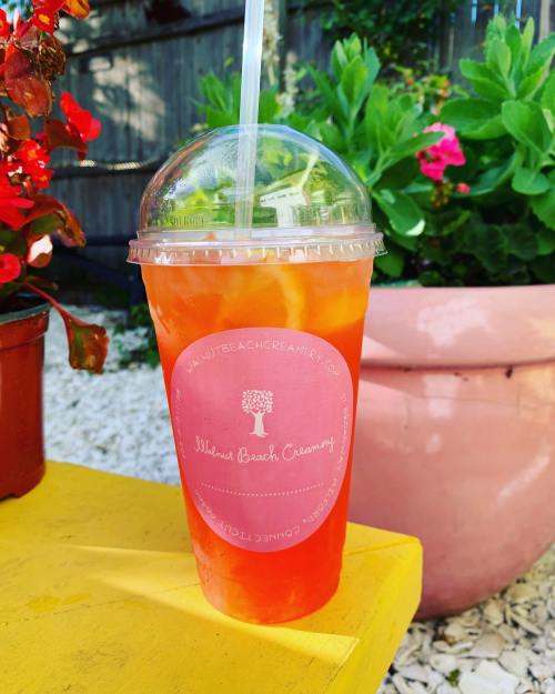 A colorful drink in a clear cup with a dome lid, placed on a yellow table near vibrant flowers.