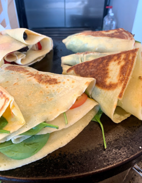 A close-up of freshly made crepes filled with spinach and tomatoes, cooking on a griddle.