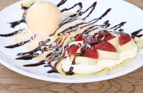 A delicious dessert plate featuring a crepe filled with bananas and strawberries, topped with whipped cream and ice cream.