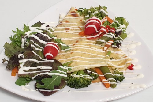 A plate of crepes topped with vegetables and drizzled with sauce, surrounded by a colorful salad.