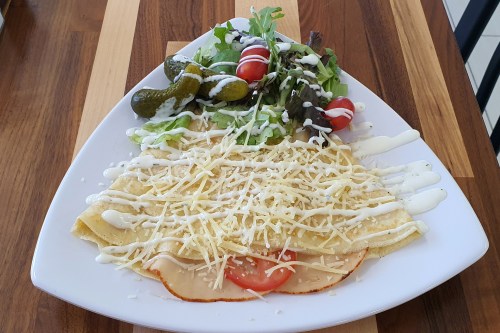 A plate of cheese-filled crepes topped with shredded cheese, accompanied by a fresh salad and pickles.