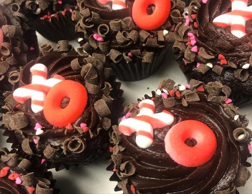 Close-up of chocolate cupcakes topped with swirls of frosting, red and pink candy, and chocolate shavings.