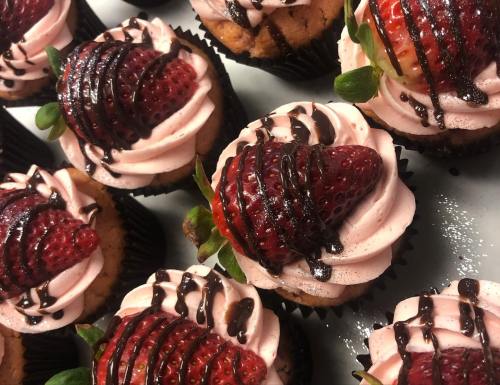 Close-up of cupcakes topped with pink frosting, fresh strawberries, and drizzled chocolate.