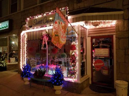 A cozy bakery storefront decorated with colorful lights and festive ornaments, featuring a welcoming sign and a cheerful atmosphere.