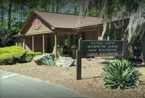 A wooden building with signs for a visitors center and camper registration, surrounded by greenery and rocks.