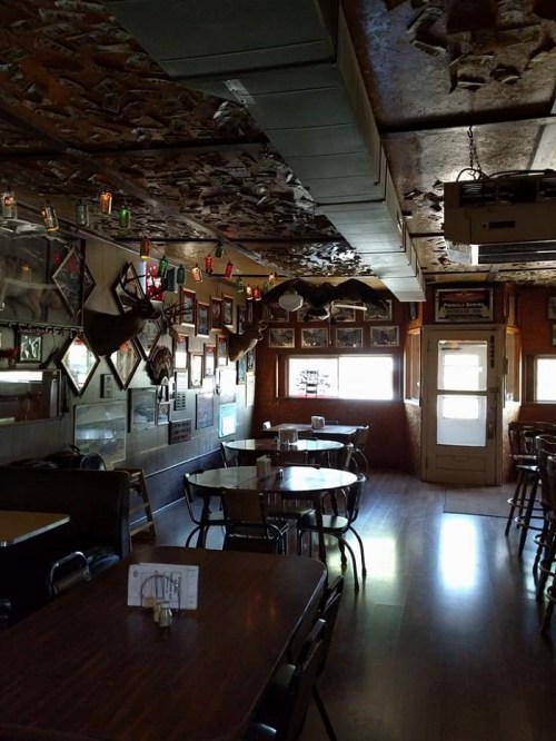 Interior of a rustic restaurant with wooden tables, framed photos on the walls, and a ceiling decorated with memorabilia.