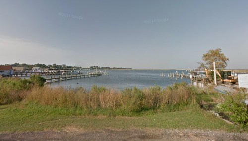 A calm waterfront scene with docks, boats, and grassy areas under a clear sky.