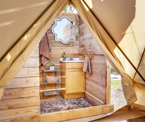 Interior of a cozy tent featuring a wooden sink, mirror, and decorative towels, with a soft rug on the floor.