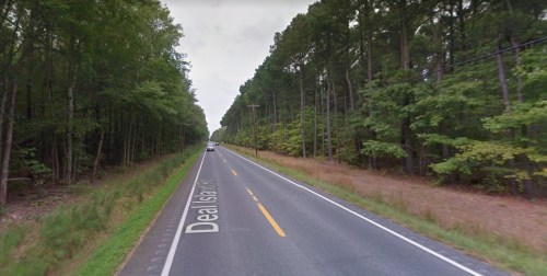 A two-lane road lined with trees, leading into the distance under a cloudy sky.