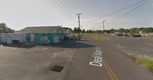 A quiet street view showing a small building and parked cars, with power lines overhead and a clear sky.