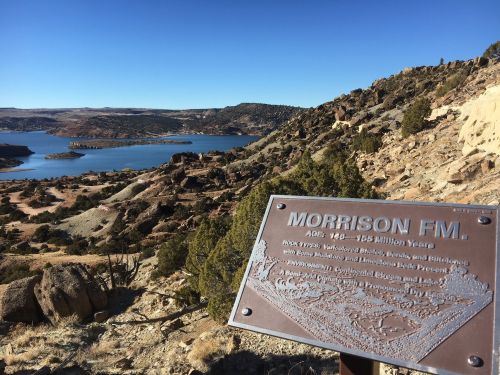 A scenic view of a lake surrounded by rocky terrain, with a sign about the Morrison Formation in the foreground.