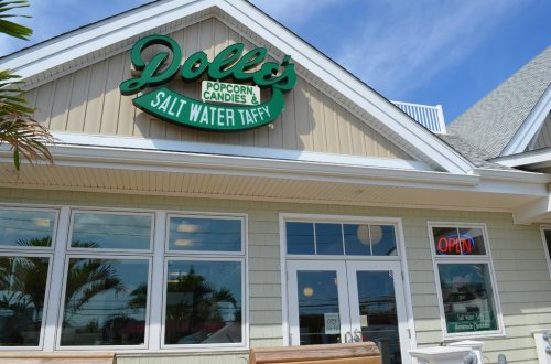 Sign for Dolle's Popcorn Candies & Salt Water Taffy on a light-colored building with an "Open" sign in the window.