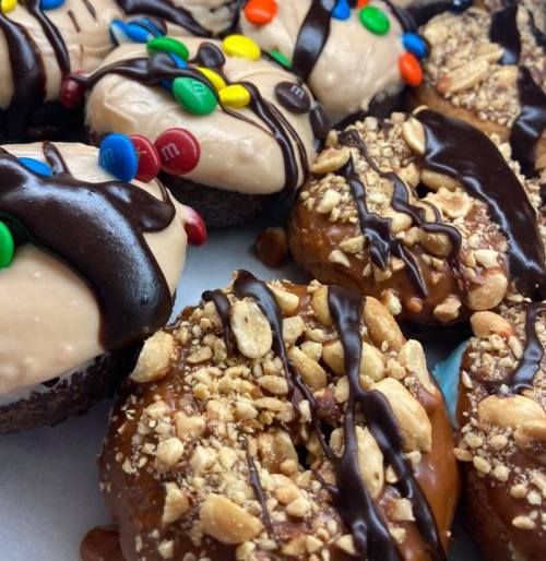 A close-up of assorted donuts topped with chocolate, peanut butter frosting, and colorful candy pieces.