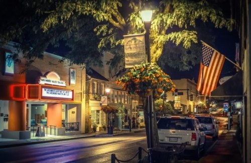 A charming street at night, featuring a theater marquee, American flag, and hanging flower baskets.