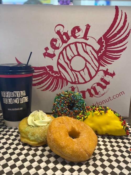 A colorful assortment of donuts and a drink, featuring sprinkles, frosting, and a donut-shaped taco, on a checkered surface.