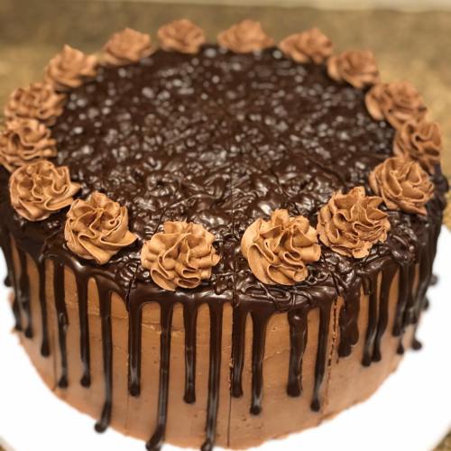 A round chocolate cake with chocolate frosting, topped with rosettes and drizzled with chocolate ganache.