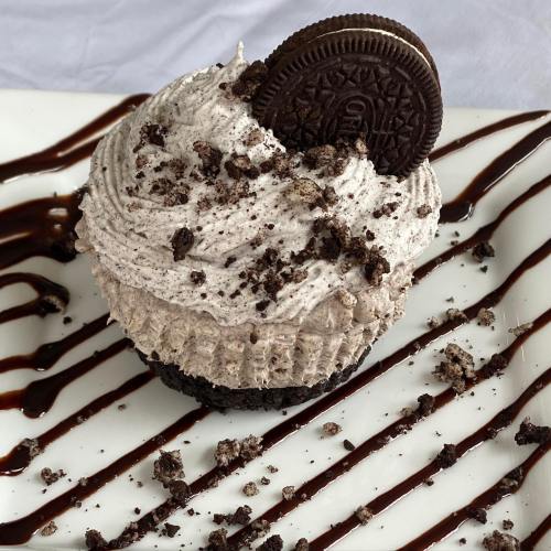 A chocolate cupcake topped with cookies and cream frosting, garnished with crushed Oreos and a whole Oreo cookie.