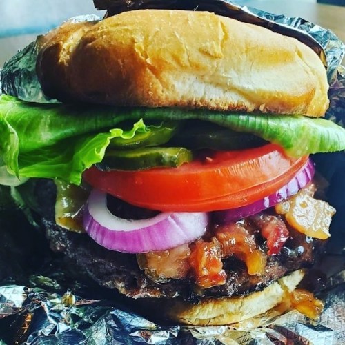 A close-up of a juicy hamburger with lettuce, tomato, pickles, red onion, and sauce, served in a bun.