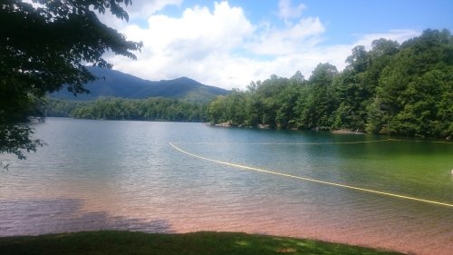A serene lake surrounded by lush green trees and mountains under a partly cloudy sky.