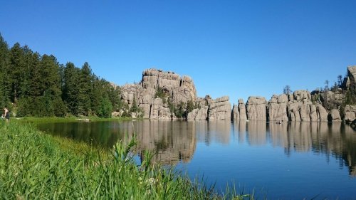 A serene lake surrounded by tall rock formations and lush green trees under a clear blue sky.