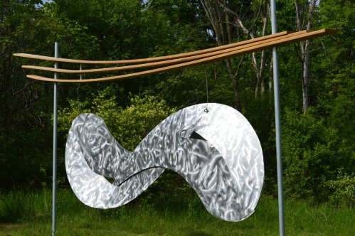 A metallic infinity sculpture hangs from wooden beams, surrounded by lush greenery.