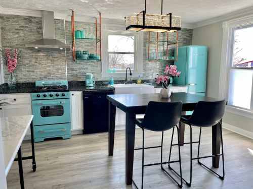 Modern kitchen with teal accents, black appliances, a large table, and decorative flowers. Bright and inviting space.