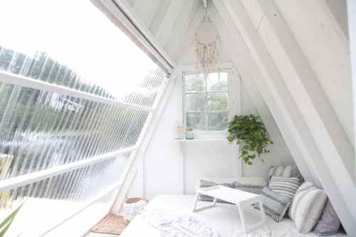 Cozy, bright interior of a small A-frame cabin with a bed, plants, and a window overlooking a serene outdoor view.