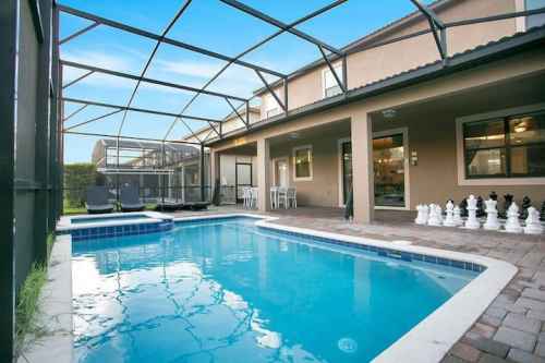 A backyard pool area with a screened enclosure, featuring a blue pool, patio furniture, and a chess set.