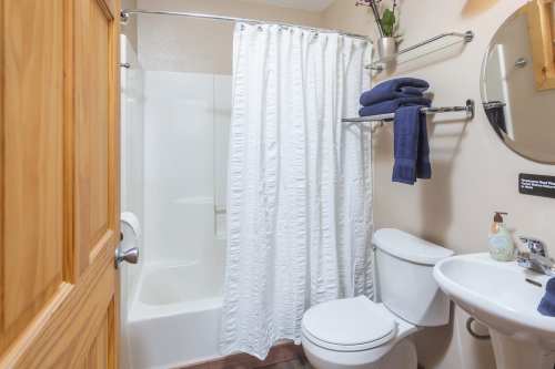 A small bathroom featuring a shower with a curtain, toilet, sink, and neatly arranged towels on a rack.