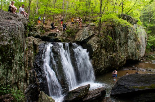 A scenic waterfall surrounded by lush greenery, with people enjoying the area and relaxing on the rocks.