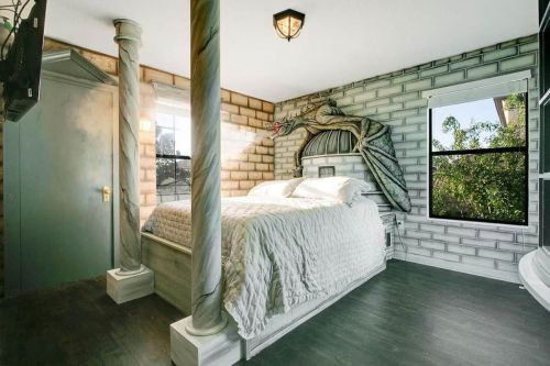 A creatively designed bedroom with a bed, stone wall murals, and a unique dragon sculpture above the headboard.