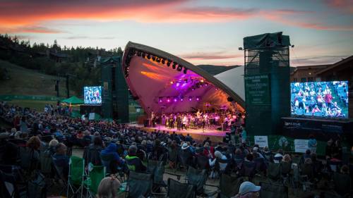 A vibrant outdoor concert at sunset, with a large audience enjoying a performance under colorful lights.