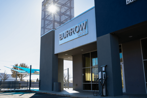 Exterior of Burrow Cafe with a charging station, sun shining in the background, and modern architectural design.