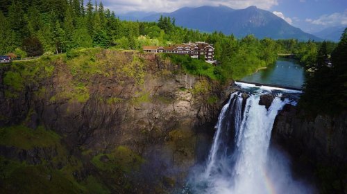 A stunning waterfall cascades down rocky cliffs, surrounded by lush greenery and mountains in the background.