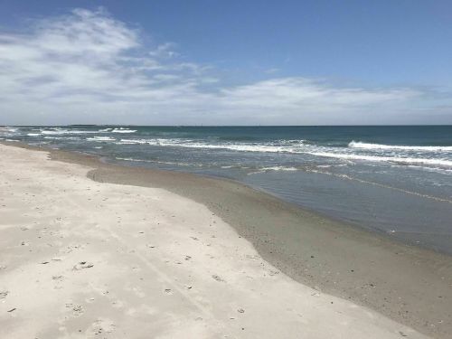 A serene beach scene with gentle waves, soft sand, and a clear blue sky.