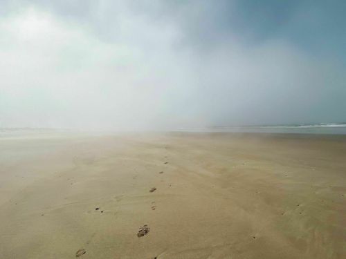 A foggy beach scene with footprints in the sand leading towards the ocean, creating a serene and mysterious atmosphere.