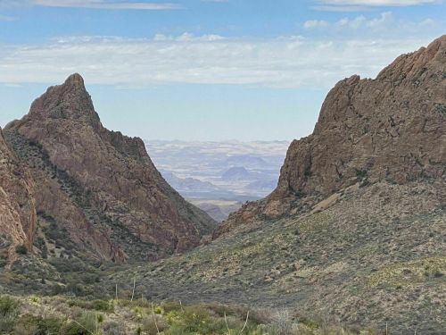 A scenic view of rugged mountains with a valley stretching into the distance under a blue sky with scattered clouds.