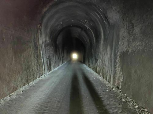 A dark tunnel with a light at the end, featuring a gravel path and textured walls.