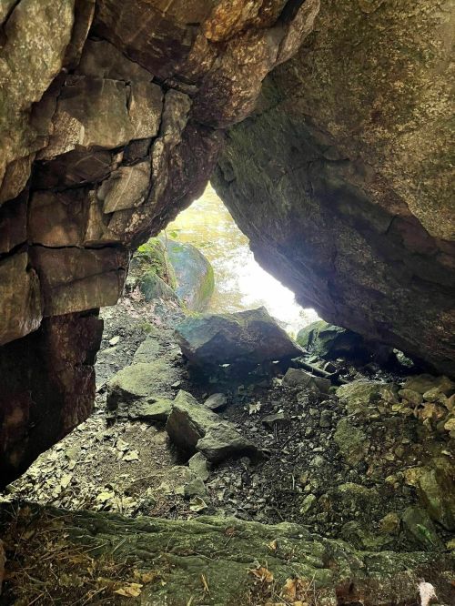 View from inside a rocky cave, looking out towards a body of water surrounded by greenery.