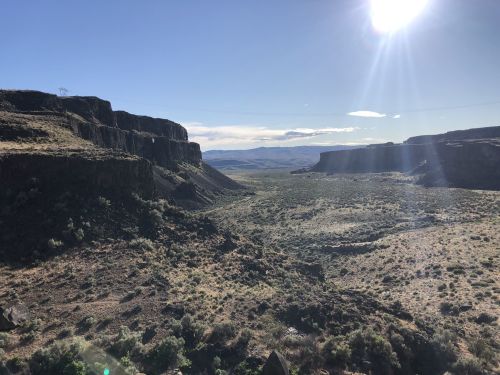 A vast landscape featuring rocky cliffs, open plains, and a bright sun shining in a clear blue sky.