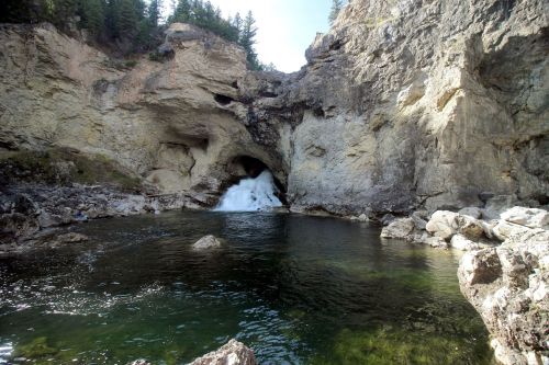 A serene natural scene featuring a waterfall cascading into a clear pool surrounded by rocky cliffs and trees.